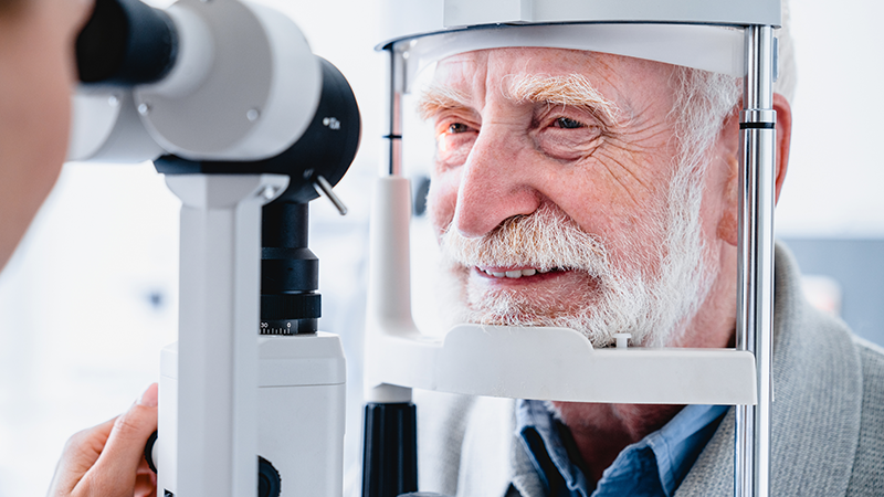 Optometrist checking older adult male's sight with slit lamp